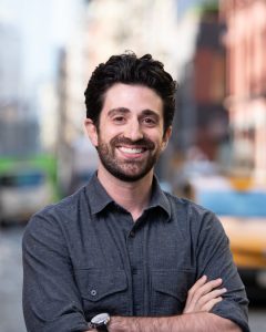 Photo of the author standing with crossed arms and smiling, with an urban background.