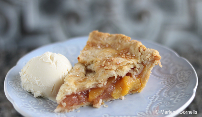 A slice of peach pie with a scoop of vanilla ice cream on a pale blue plate.